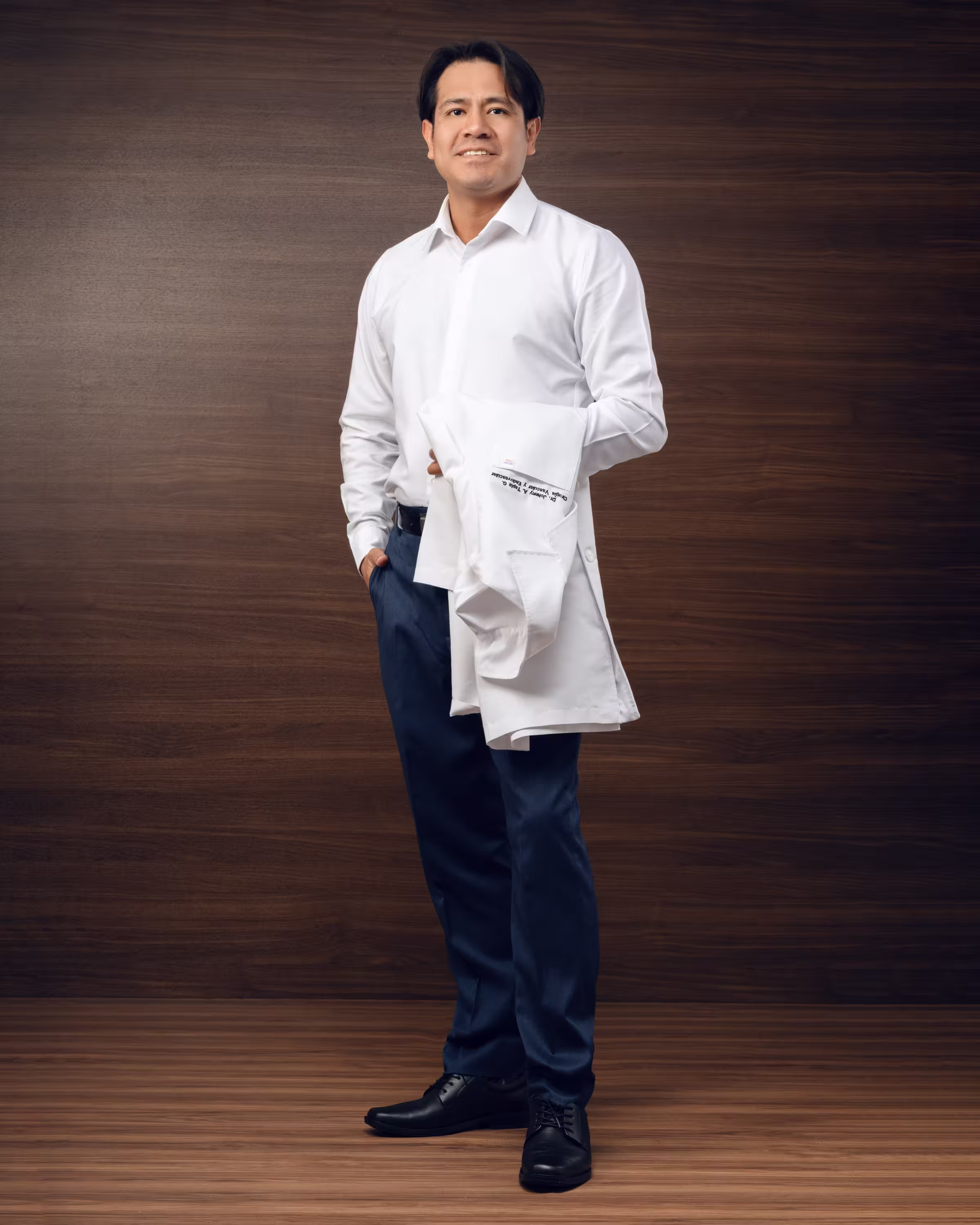 El Dr. Johnny Tapia de pie, con camisa blanca y su bata médica en el brazo